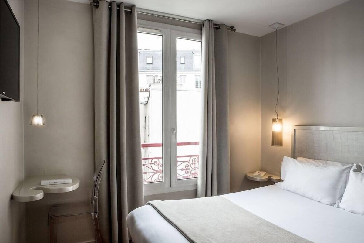 A hotel room with a bed, bedside table, and a window with curtains.