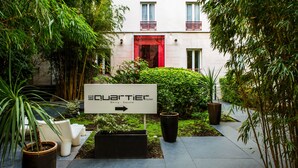 A sign for the Quartier Hotel pointing to the right, surrounded by greenery and potted plants. - Hôtel Le Quartier Bercy Square (Paris)