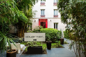 A sign for the Quartier Hotel pointing to the right, surrounded by greenery and potted plants.