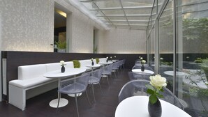 A modern outdoor seating area with white benches and round tables, some with vases of flowers. - Hôtel Le Quartier Bercy Square (Paris)