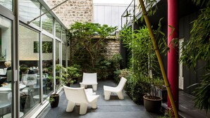 A modern outdoor seating area with white chairs and tables, surrounded by potted plants and a stone wall. - Hôtel Le Quartier Bercy Square (Paris)