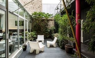 A modern outdoor seating area with white chairs and tables, surrounded by potted plants and a stone wall.