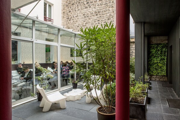 An outdoor seating area with white benches and potted plants, overlooking a busy street with people and cars. - Hôtel Le Quartier Bercy Square (Paris)