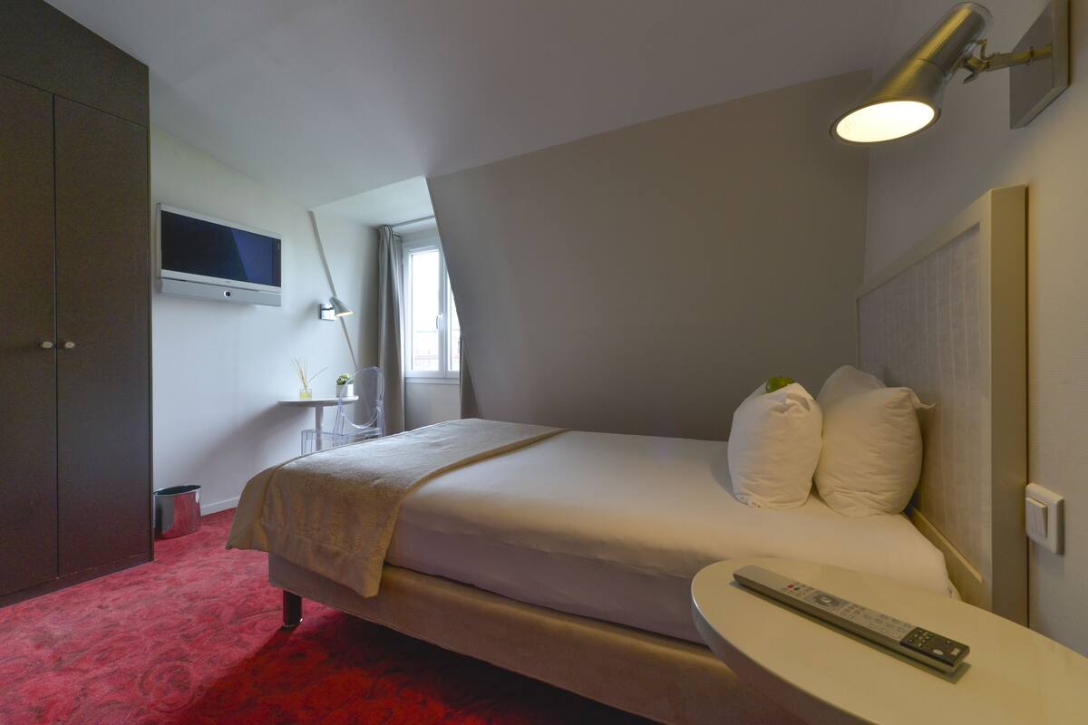 A hotel room with a bed, bedside table, and a TV mounted on the wall.