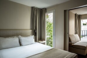 A hotel room with a bed, a chair, a small table, and a view of greenery outside. - Hôtel Le Quartier Bercy Square (Paris)