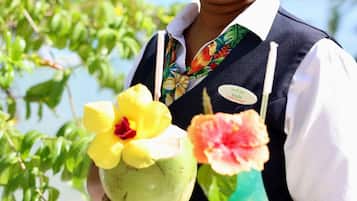 A person holding a tray with a coconut and a drink garnished with flowers.