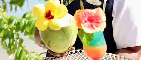 A person holding a tray with a coconut and a drink garnished with flowers.