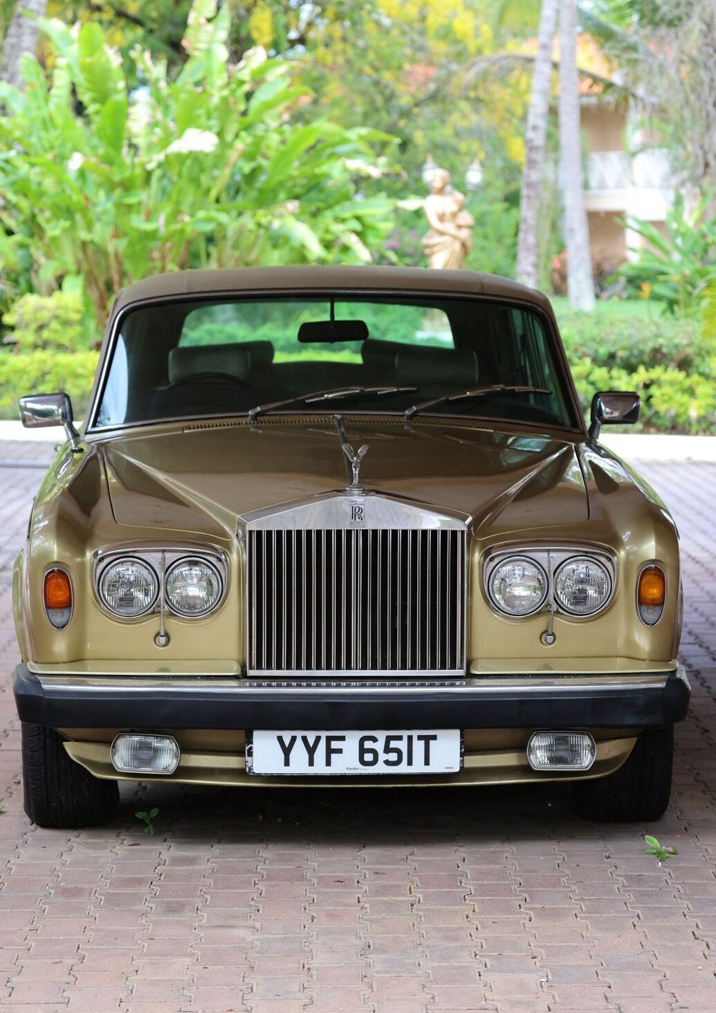 A vintage Rolls-Royce parked on a paved surface with greenery in the background.