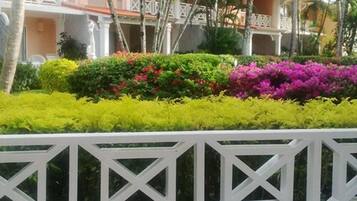 A hotel with a white balcony railing, lush green and pink bushes, and palm trees.