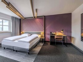 Una habitación de hotel moderna con cama, escritorio, silla y una pared de acento morada.