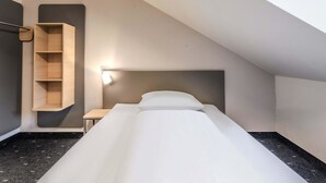 Una habitación pequeña y moderna con una cama, un estante de madera y una mesita de noche.