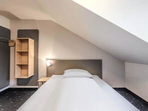 A small, modern room with a bed, a wooden shelf, and a nightstand. - B&B HOTEL Passau-Süd (Passau)