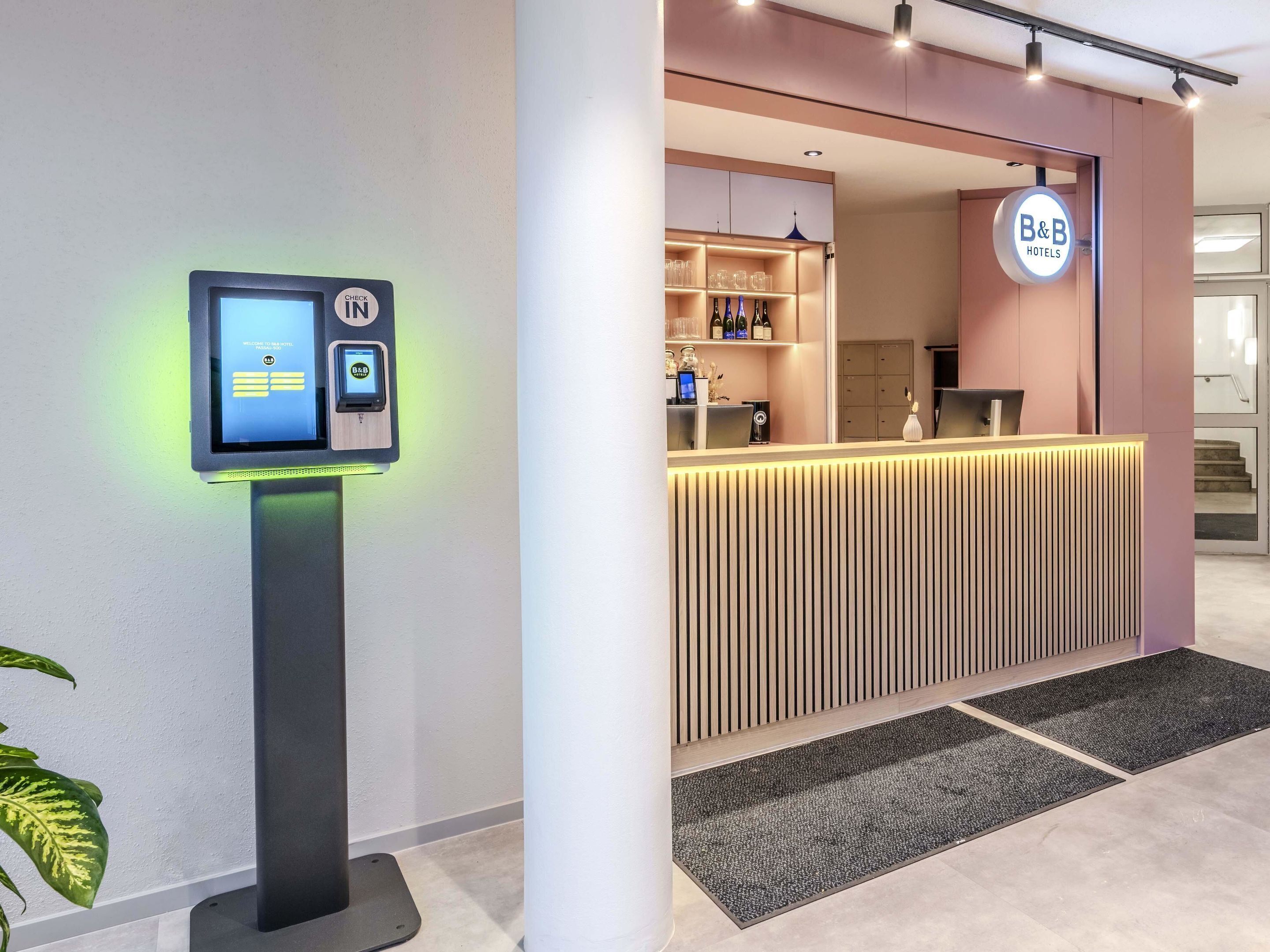 Un espace d’accueil d’hôtel comprenant un terminal d’enregistrement numérique, un comptoir d’accueil et une enseigne B&B Hotels.