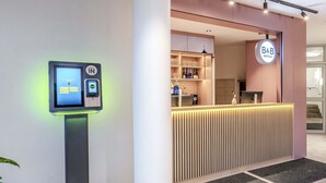 Zona de recepción de hotel con quiosco de registro digital, mostrador de recepción y cartel de B&B Hotels.