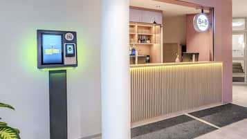 Un espace d’accueil d’hôtel comprenant un terminal d’enregistrement numérique, un comptoir d’accueil et une enseigne B&B Hotels.