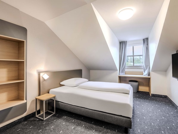 A modern, compact hotel room with a bed, bedside table, and built-in shelving.