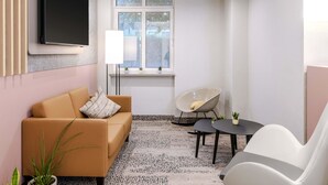 Una sala de estar moderna con un sofá, un sillón, una mesita, un televisor montado en la pared y una ventana con plantas en el alféizar.