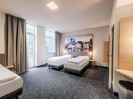 Habitación de hotel con dos camas, un ventanal con cortinas, un cuadro de paisaje urbano en la pared y una puerta a la derecha.