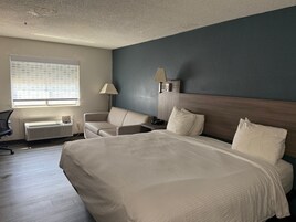 Una habitación de hotel con una cama grande, un escritorio con silla, un sofá, una lámpara y una ventana con persianas.