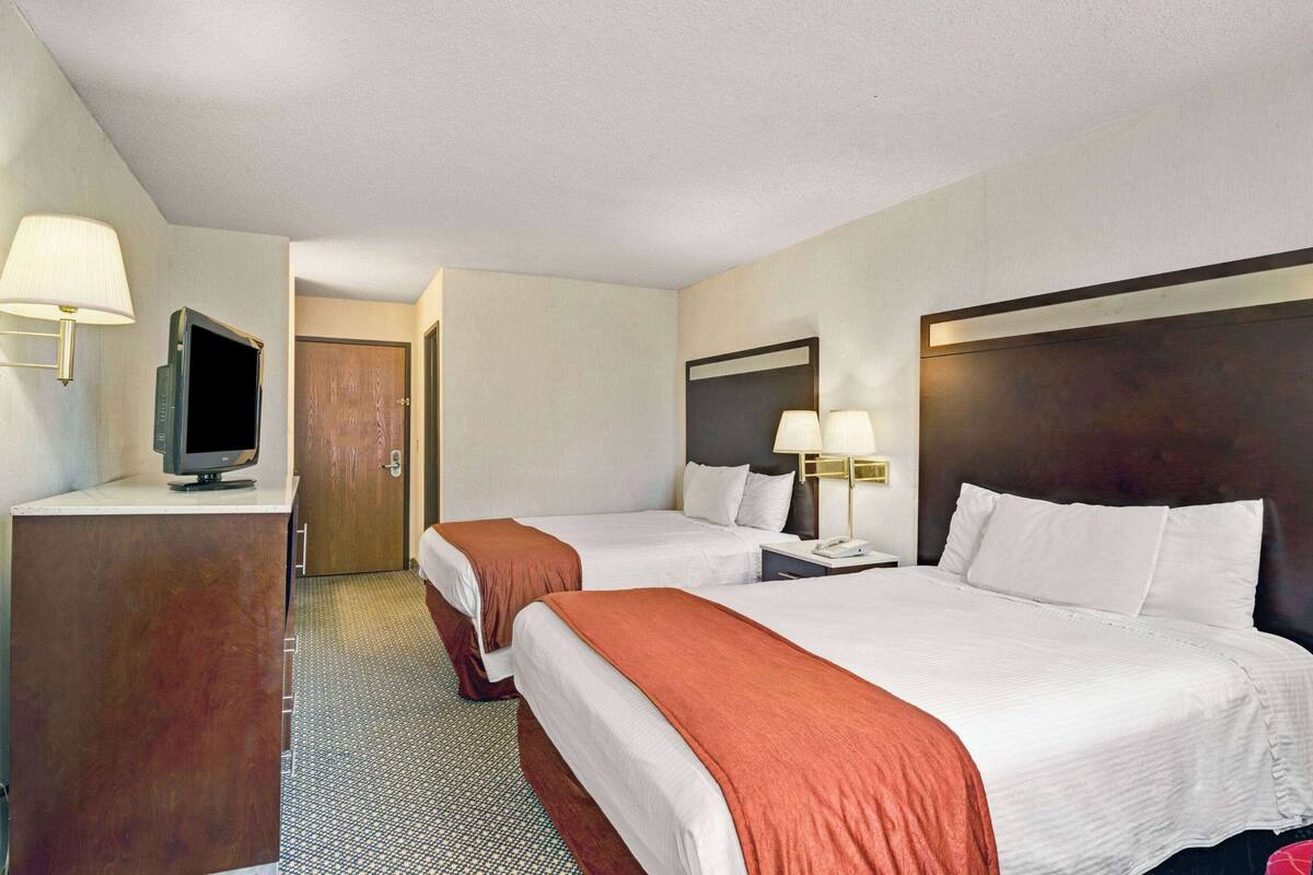 A hotel room with two beds, a desk with a television, and a door leading to another room.