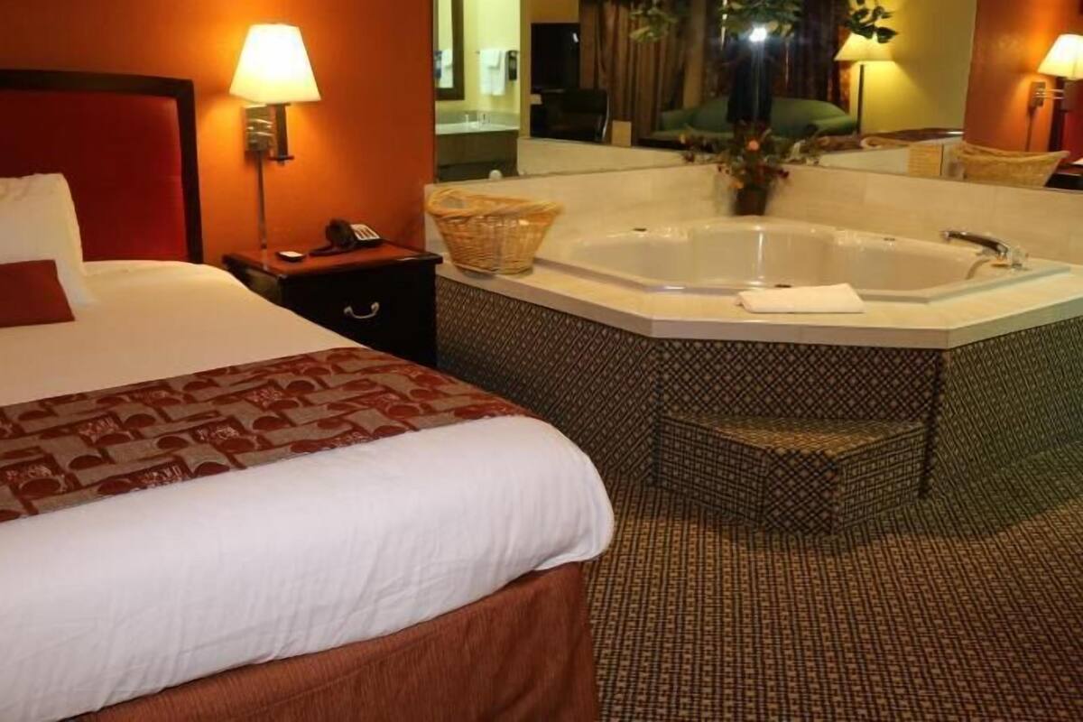 Habitación de hotel con una cama grande, baño independiente con bañera y una pequeña zona de estar.