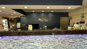 Una recepción en Baymont Inn & Suites con un mostrador de mármol oscuro, una pared decorada con mosaicos y un letrero sobre el mostrador.