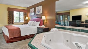 Habitación de hotel con una cama grande, zona de estar con una silla y una mesa, bañera y un espejo amplio.