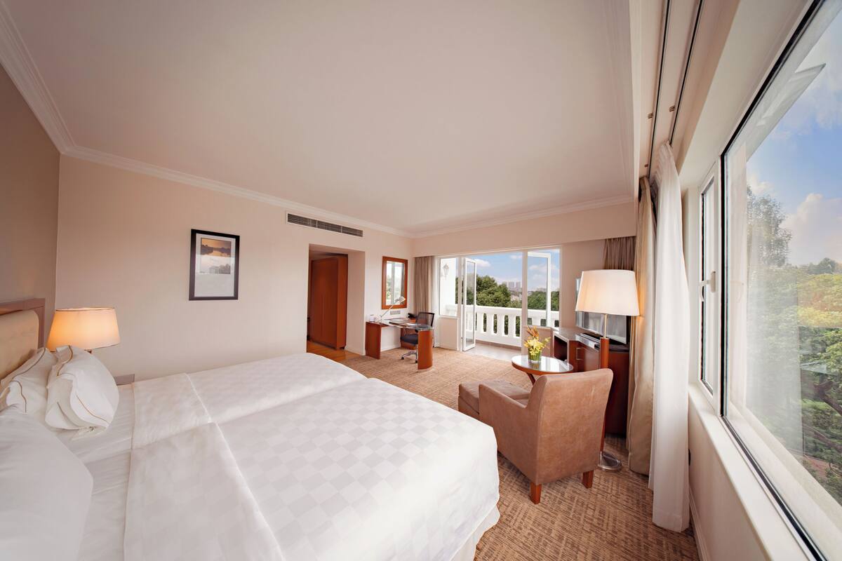 A hotel room with a large bed, a desk, a chair, and a balcony with a view.