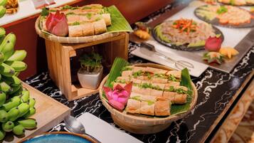 A buffet with various food items, including a dish with cubes on a banana leaf, a plate with rice and vegetables, and a bowl of green bananas.