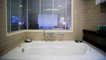 A bathroom with a bathtub, a window with blinds, and a shelf with toiletries.