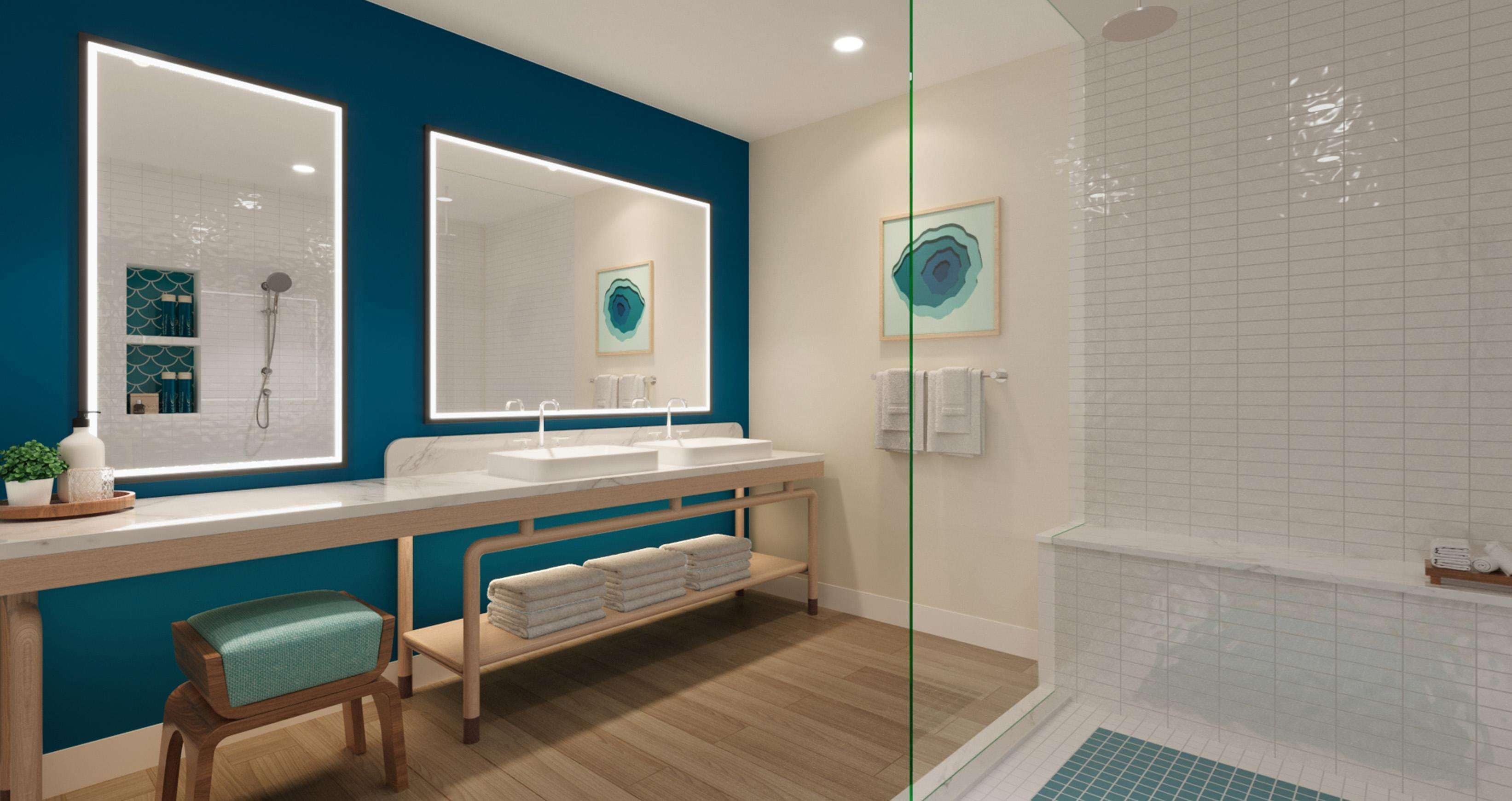 A modern bathroom with a large mirror, two sinks, a shower, and a bench with towels.