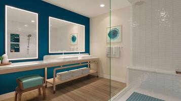 A modern bathroom with a large mirror, two sinks, a shower, and a bench with towels.