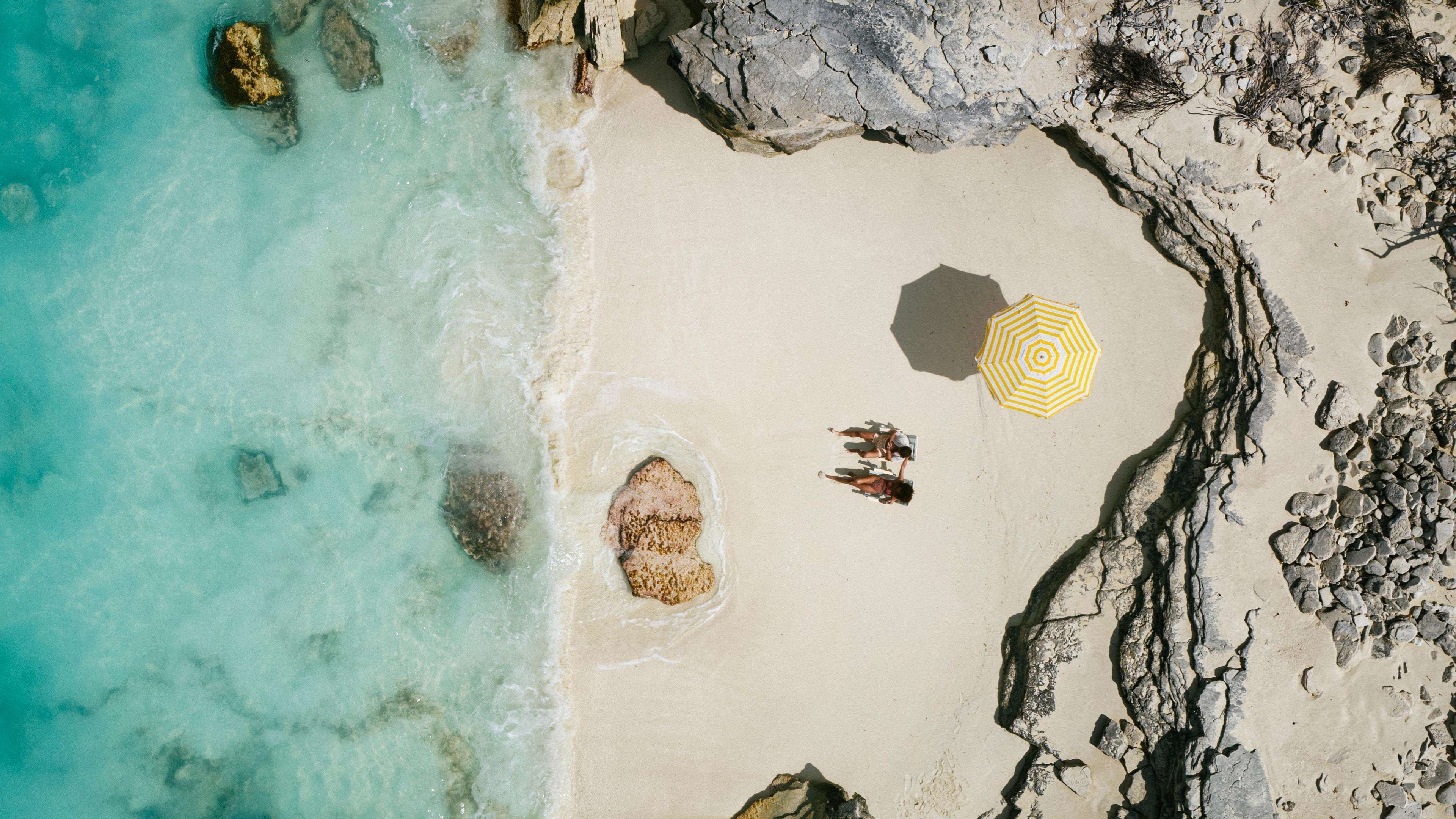 Una playa con agua turquesa cristalina, costa rocosa y un paraguas amarillo.
