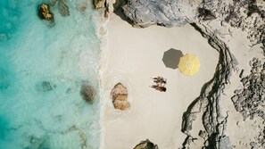 A beach with clear turquoise water, rocky shoreline, and a yellow umbrella.