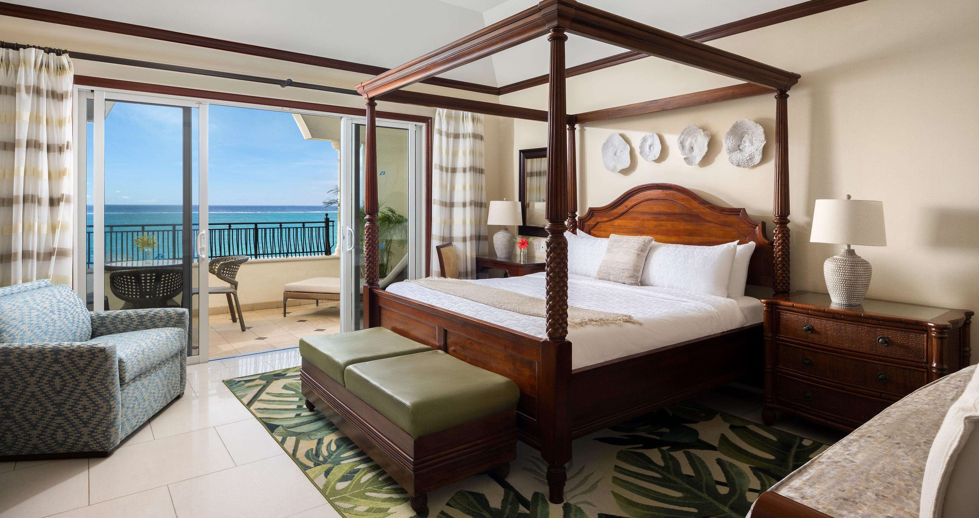 A four-poster bed with a wooden headboard, a sitting bench, a nightstand, and a lamp.