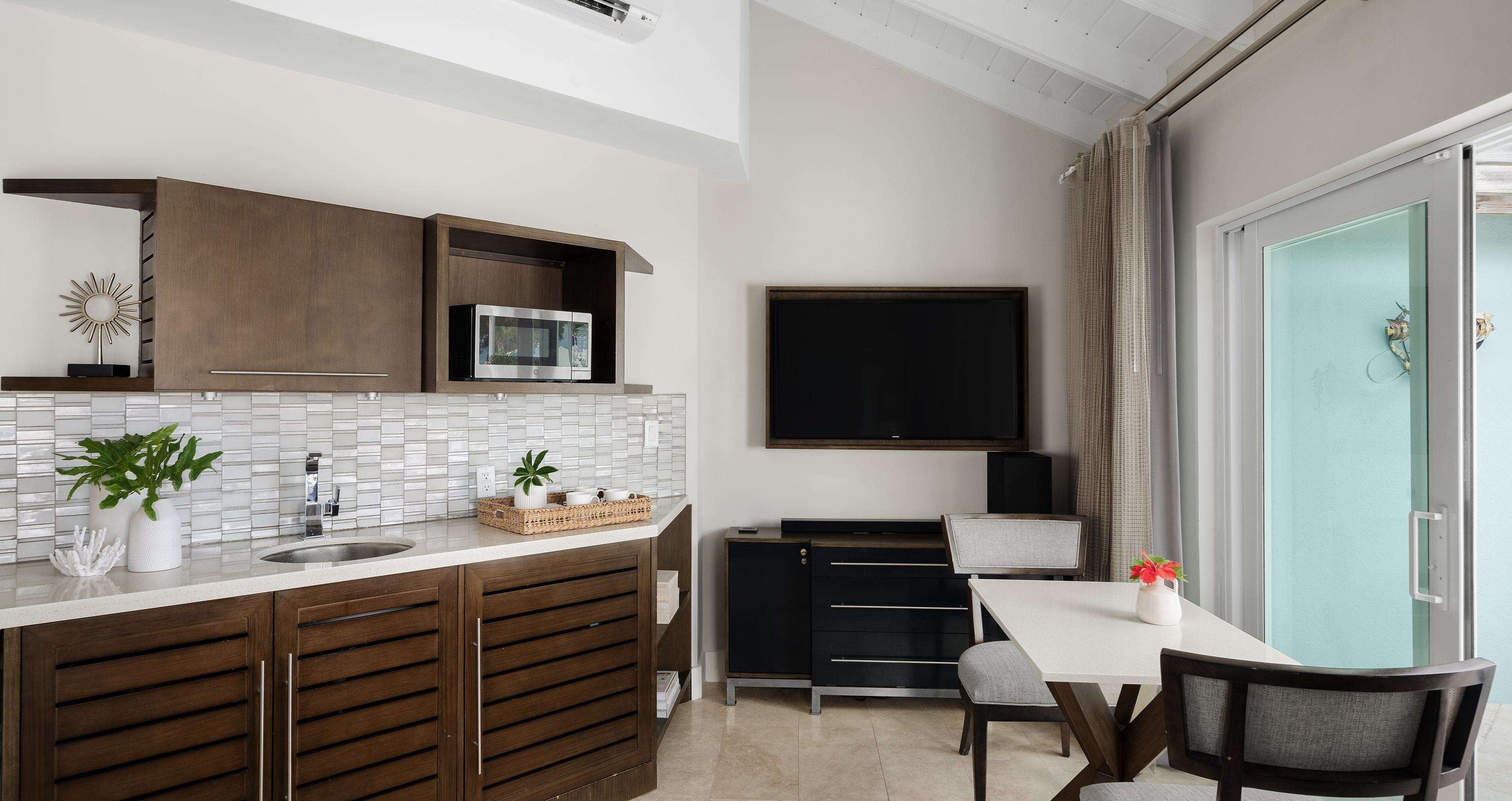 A modern kitchen with a built-in microwave, a large flat-screen TV, and a dining area with a table and chairs.