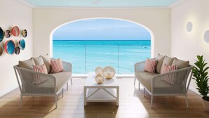 A room with two sofas facing a large arched window overlooking the sea, a coffee table with decorative items, and a wall with woven baskets.