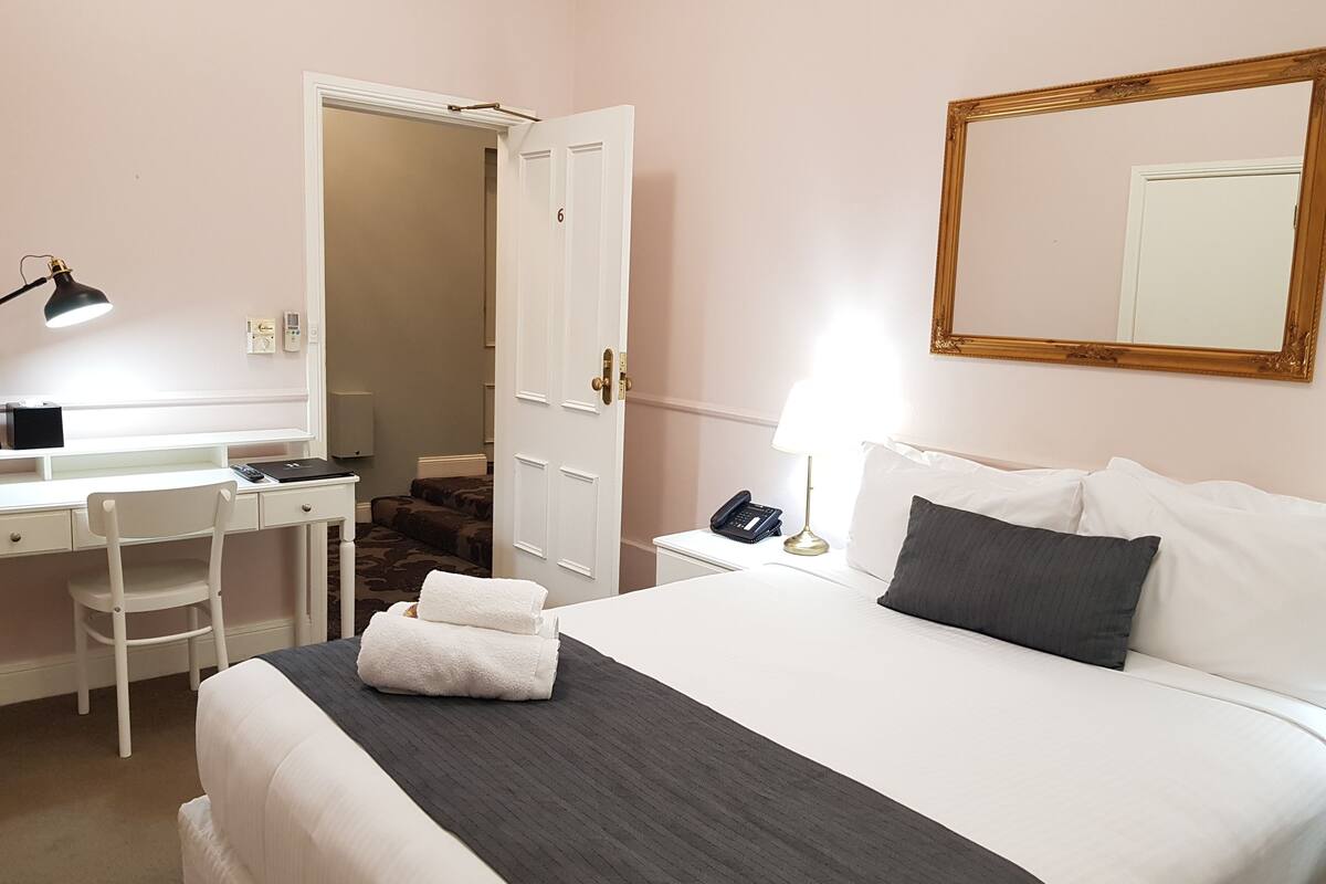 A hotel room with a bed, a desk, a chair, a lamp, a phone, and a mirror.