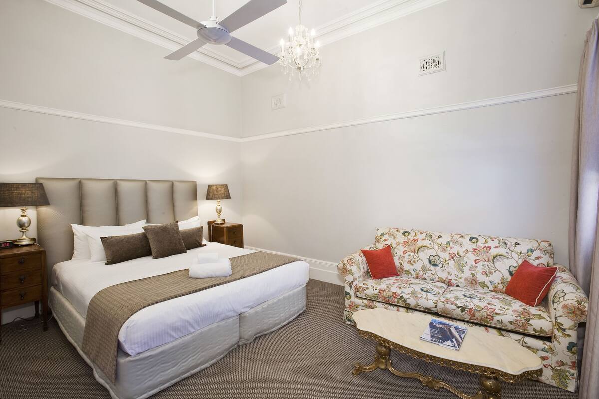 A hotel room with a large bed, a sofa, a coffee table, and a ceiling fan.