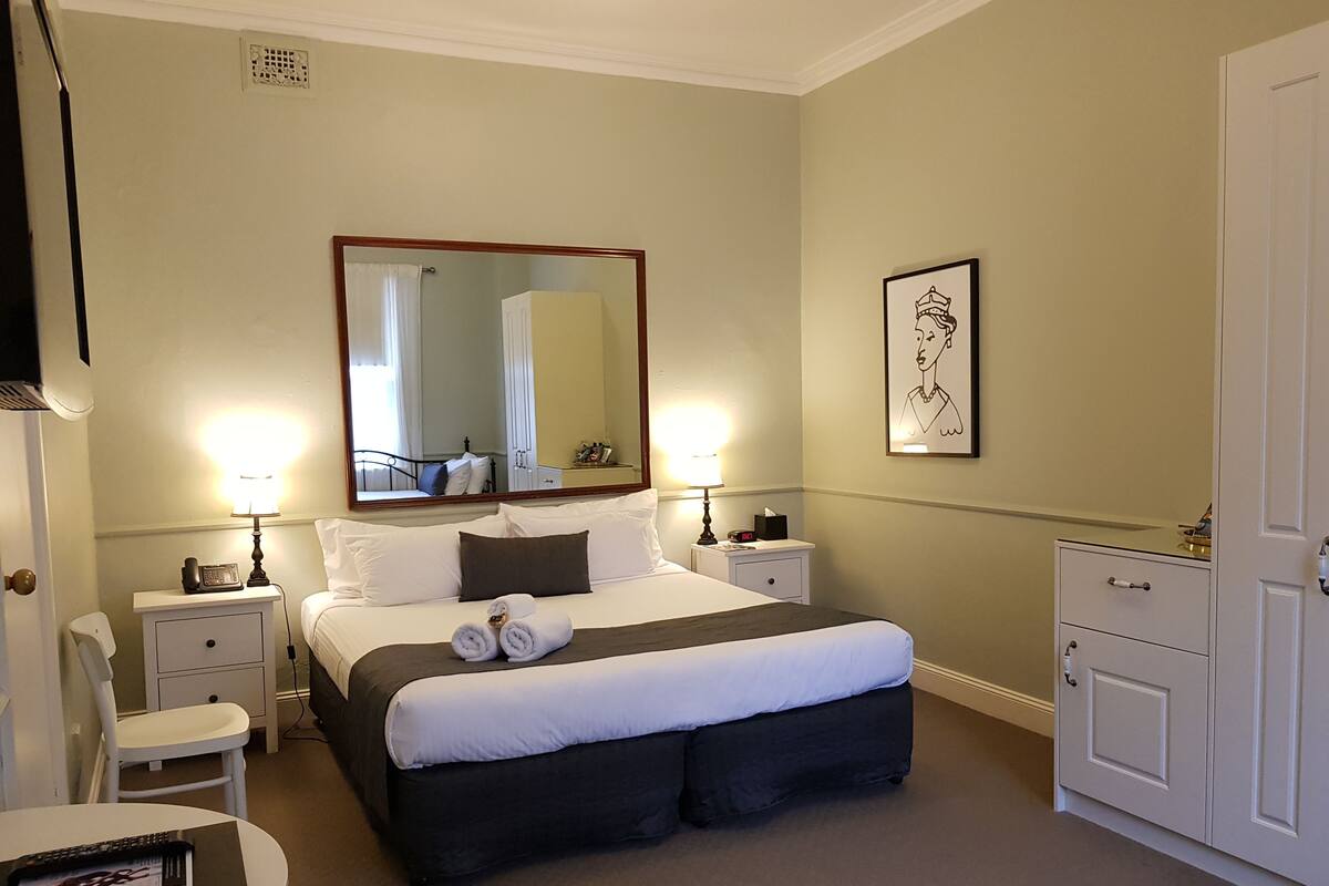 A hotel room with a large bed, two bedside tables, a nightstand, a round table, and a wardrobe.