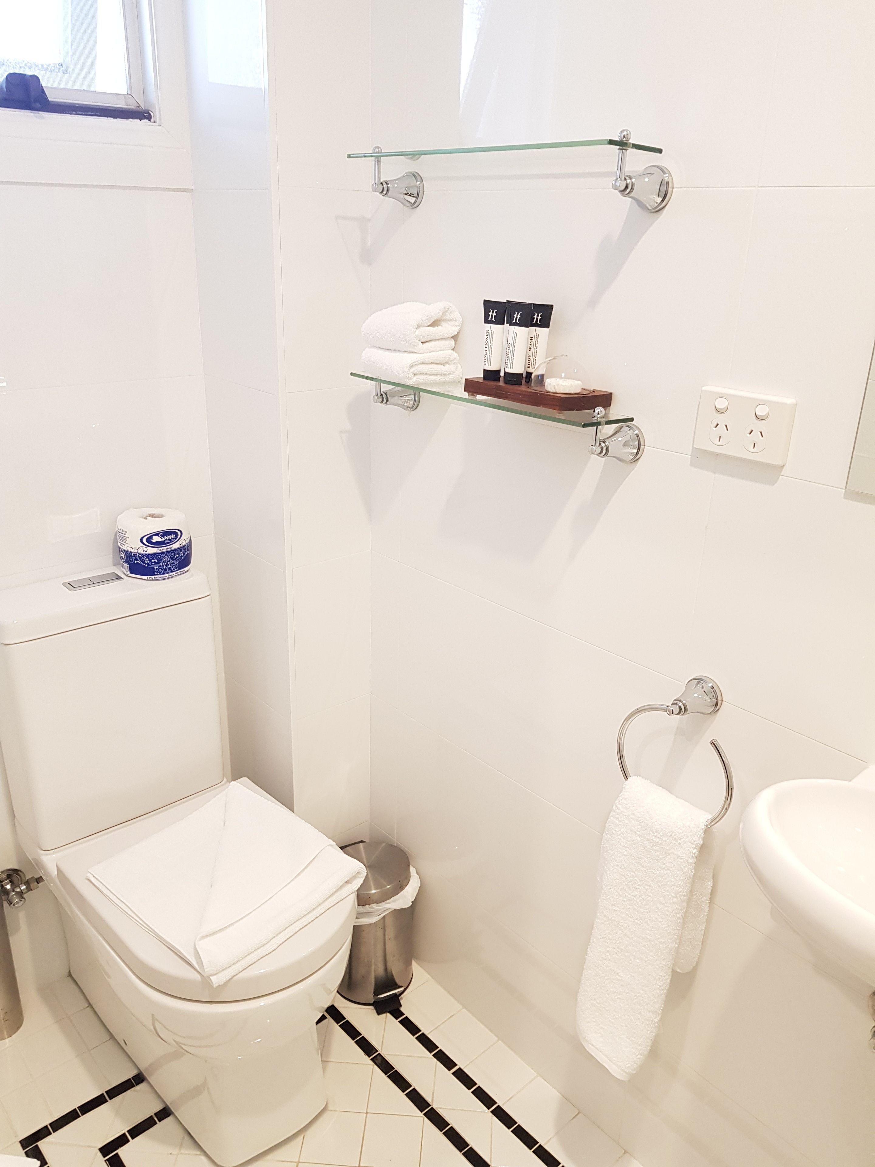 Un baño con inodoro, bidé, repisa de vidrio con artículos de aseo y lavamanos.