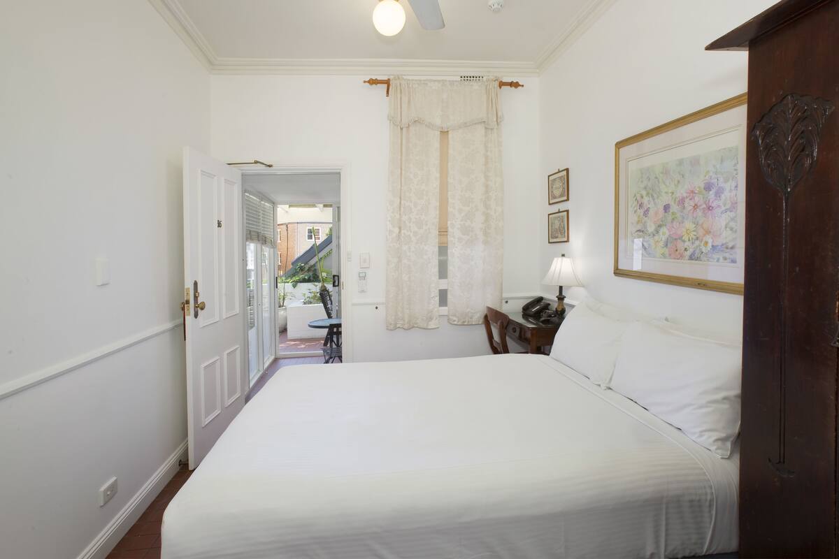 A bedroom with a bed, a desk with a lamp, a door, and a painting on the wall.