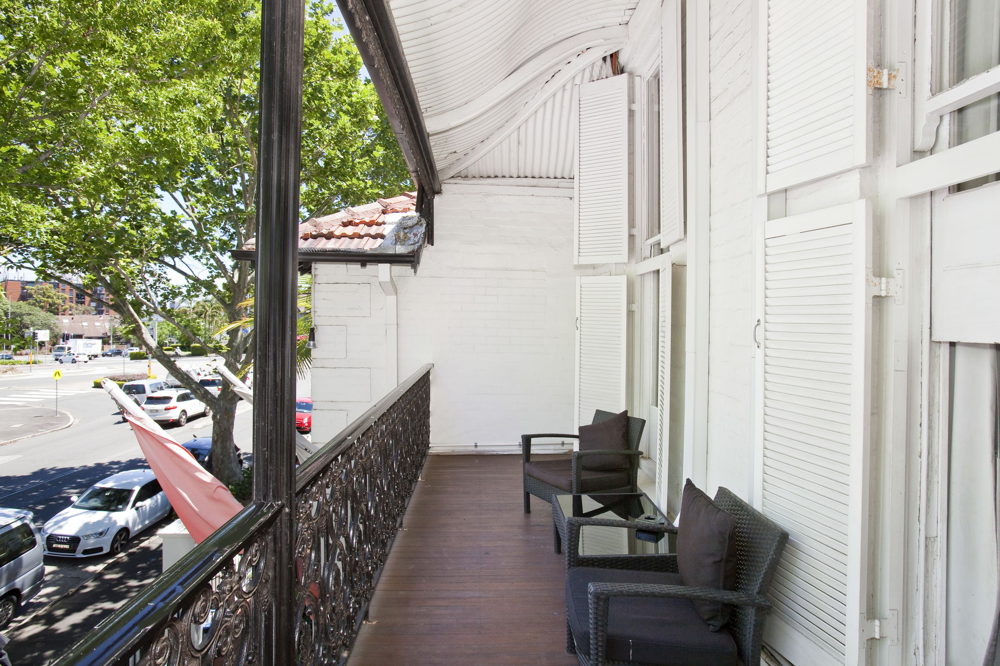 A balcony with wicker furniture and a view of parked cars and trees.