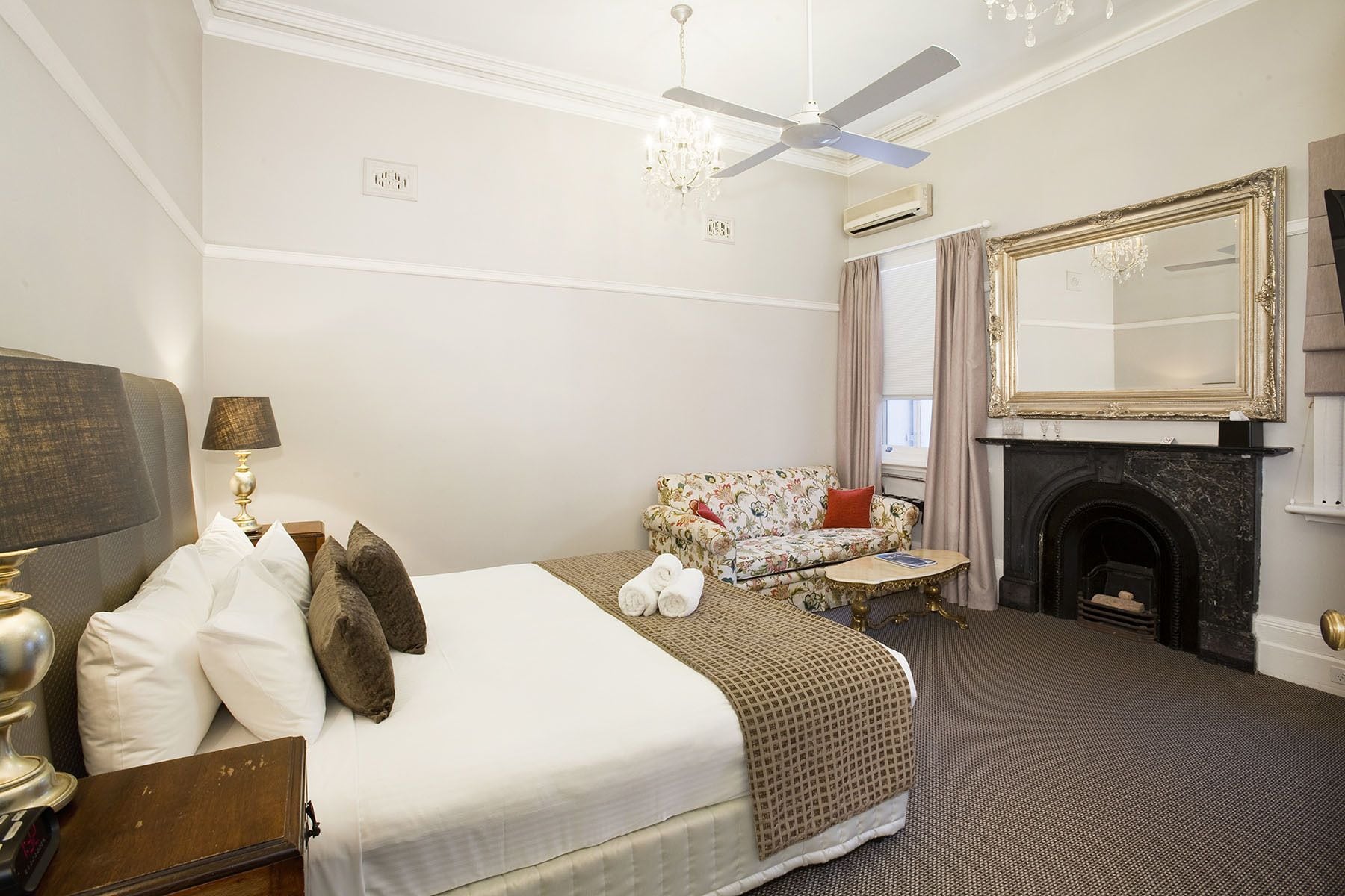 A hotel room with a bed, a sofa, a fireplace, and a large mirror.