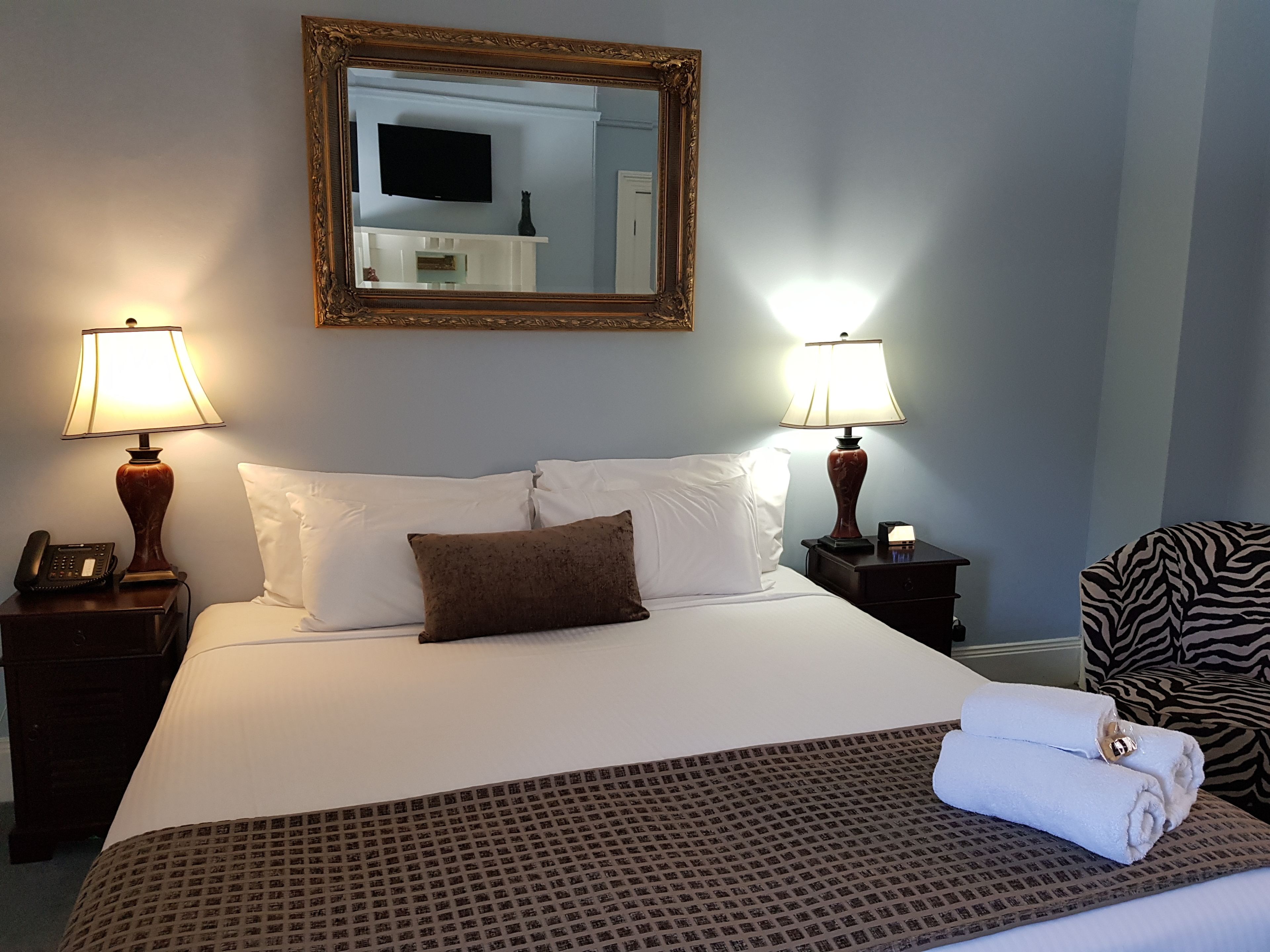 Habitación de hotel con una cama grande, dos lámparas de noche, un televisor de pantalla plana sobre la cama y una silla con estampado de cebra.