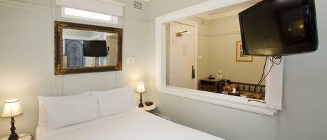 Une chambre d’hôtel avec un lit, un téléviseur fixé au mur, un miroir et une table de chevet avec une lampe.