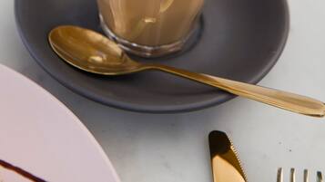 A cup of coffee with latte art on a saucer, a spoon, and a fork on a table.
