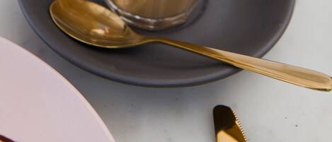 A cup of coffee with latte art on a saucer, a spoon, and a fork on a table.