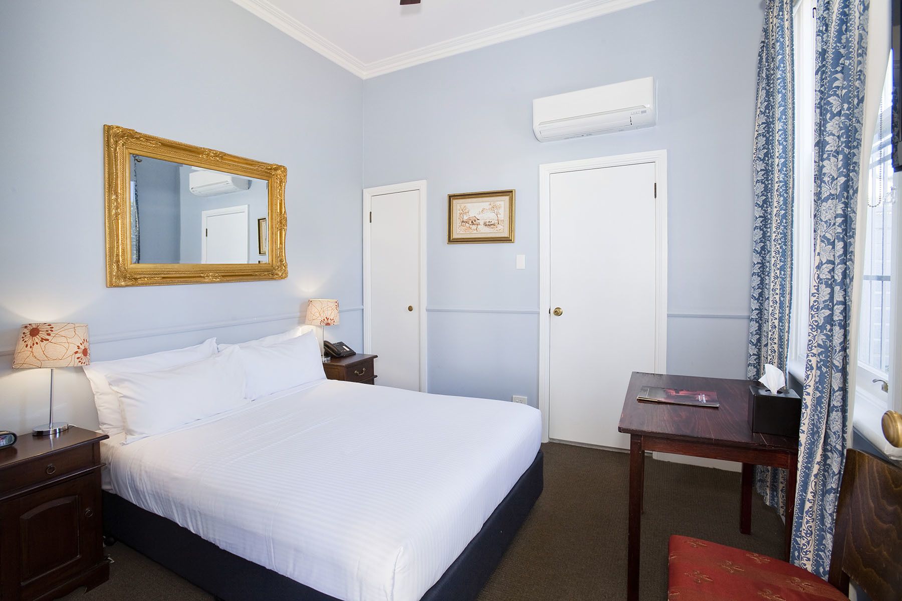 A hotel room with a large bed, a desk, a chair, a mirror, and a picture on the wall.