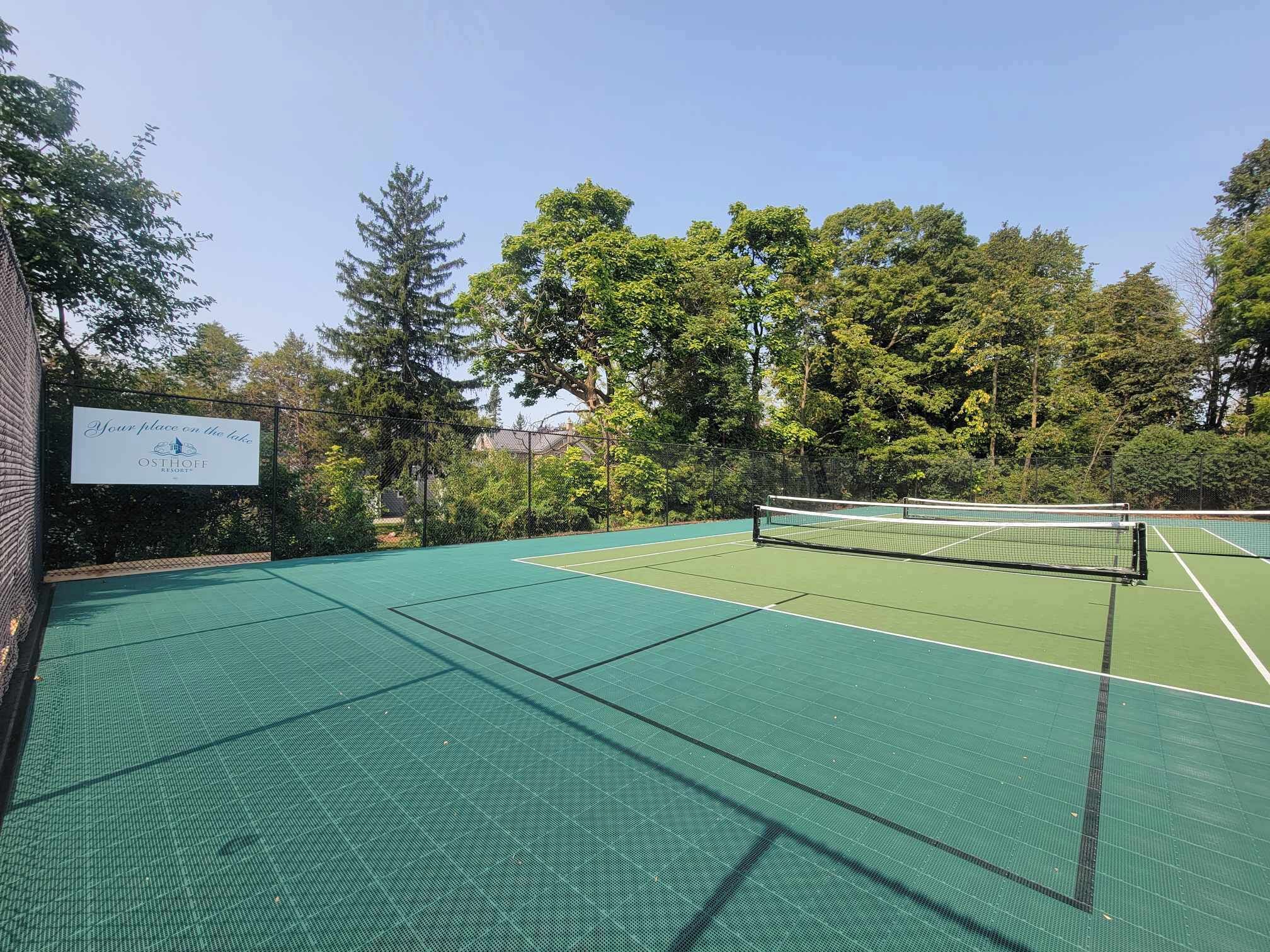 Una cancha de tenis al aire libre en el Osthoff Resort, con una red en el centro, rodeada de árboles y un cielo despejado.